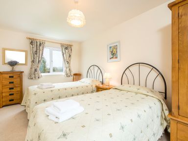 A bedroom with two single beds a wooden dresser a chair a bedside table with a lamp and a window with curtains at Cothi Cottage Cardigan Near Cenarth