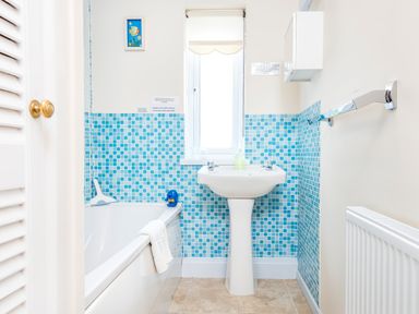 A bathroom with a bathtub towel and shower squeegee a pedestal sink and blue tile walls at Cothi Cottage Cardigan Near Cenarth