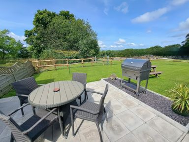 An outdoor patio garden with a round table and four chairs a barbecue grill a picnic bench and a green lawn at Cothi Cottage in Cardigan Near Cenarth