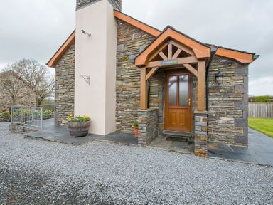 The stone exterior of a house with a wooden door and a small covered porch at Hirwaun Cottage Cardigan Near Cenarth