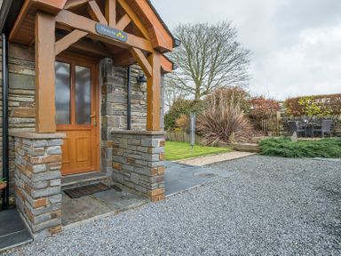 A stone and wood entrance door with a small covered porch and a gravel driveway and garden area at Hirwaun Cottage Cardigan Near Cenarth