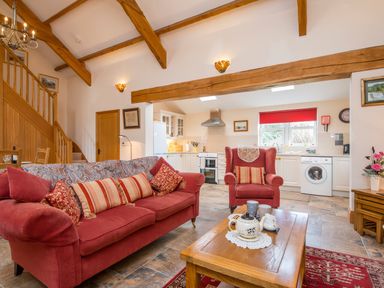 An open living room and kitchen with red sofa and armchair wooden beams and staircase at Hirwaun Cottage Cardigan Near Cenarth