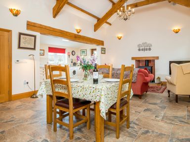 A dining area with wooden chairs and a table with a floral tablecloth next to a living room with sofas and a fireplace at Hirwaun Cottage Cardigan near Cenarth