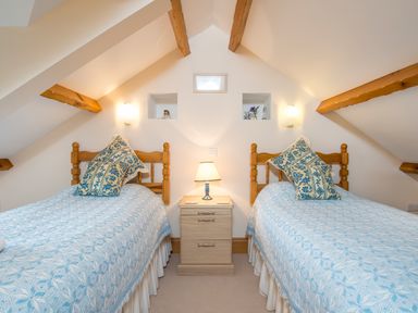 A bedroom with two single beds with blue bedspreads and patterned pillows separated by a wooden nightstand with a lamp at Hirwaun Cottage in Cardigan Near Cenarth