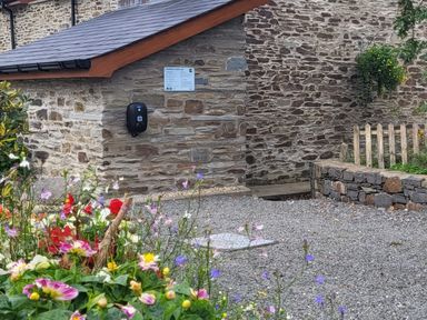 A stone building with an electric car charging point and a garden with colorful flowers at Hirwaun Cottage in Cardigan Near Cenarth