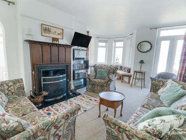 A living room with patterned sofas a wooden fireplace and a wall mounted TV at The Harbour in Rhosneigr