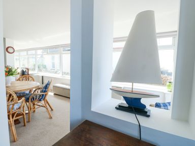 A dining area with a round wooden table and chairs and a sailboat lamp on a shelf at The Harbour in Rhosneigr