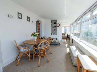 A dining area with a wooden table and rattan chairs beside a long window at The Harbour in Rhosneigr