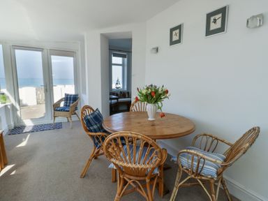 A dining area with a round wooden table surrounded by wicker chairs with cushions and a vase of flowers on the table at The Harbour in Rhosneigr
