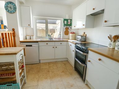 A kitchen with white cabinets wooden countertops and a window above the sink at The Harbour in Rhosneigr