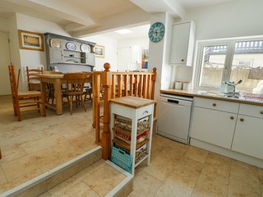 A kitchen and dining area with wooden furniture and white cabinets at The Harbour in Rhosneigr