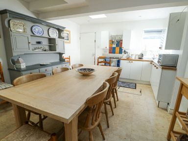 A kitchen with a wooden dining table and chairs and a gray cabinet with plates on display at The Harbour in Rhosneigr