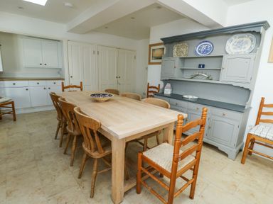 A dining room with a wooden table and chairs and a grey cabinet with plates on the shelves at The Harbour in Rhosneigr