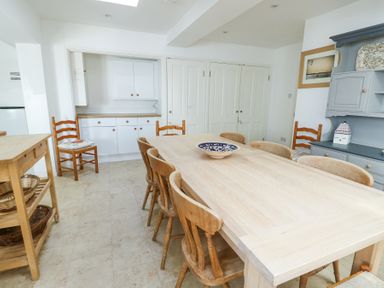 A dining room with a long wooden table surrounded by chairs and a blue cabinet on the right at The Harbour in Rhosneigr