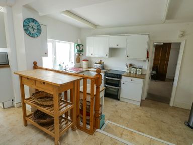 A kitchen with wooden island, white cabinets, oven, sink under window, and utensils at The Harbour in Rhosneigr