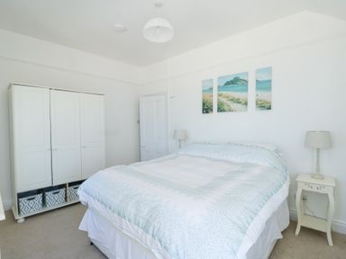 A bedroom with a double bed bedside tables lamps wardrobe and three panel paintings on the wall at The Harbour in Rhosneigr