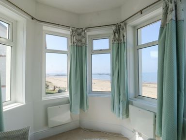 A corner room with three windows and green curtains overlooking a sandy beach at The Harbour in Rhosneigr