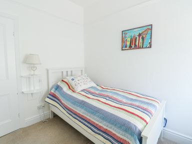 A small bedroom with a single bed a striped quilt a pillow a wall lamp and a surfboard picture at The Harbour in Rhosneigr