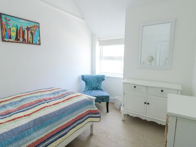 A bedroom with a striped bedspread a blue patterned chair a white cabinet and a mirror at The Harbour in Rhosneigr