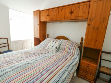 A bedroom with a wooden bed and storage units a striped bedspread and two wooden chairs at The Harbour in Rhosneigr