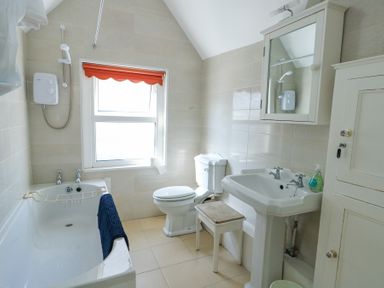 A bathroom with a bathtub shower toilet sink mirror cabinet stool and window at The Harbour in Rhosneigr