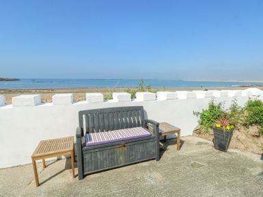 A bench with cushion between two wooden side tables near a white wall overlooking a beach at The Harbour in Rhosneigr
