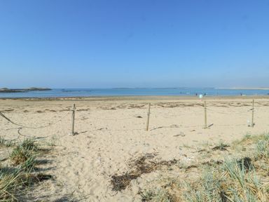 A sandy beach with wooden posts and rope fence and people near the water at The Harbour in Rhosneigr
