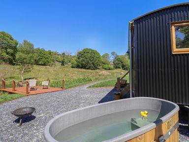 An outdoor area with a hot tub containing a rubber duck next to a black corrugated building and a deck with two chairs at Celyn in Bontddu near Dolgellau
