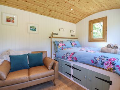 A bedroom with a floral bedspread a brown sofa and framed pictures on the wall at Celyn in Bontddu near Dolgellau
