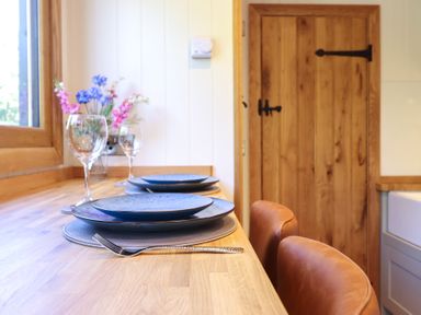 A wooden countertop with blue plates, wine glasses, and flowers near a wooden door at Celyn in Bontddu near Dolgellau