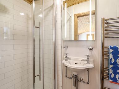 A bathroom with a glass shower enclosure a white sink with two taps a mirror and a towel on a heated rail at Celyn in Bontddu near Dolgellau