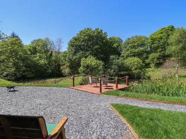 An outdoor seating area with two chairs on a wooden deck surrounded by grass trees and a gravel path at Celyn in Bontddu near Dolgellau