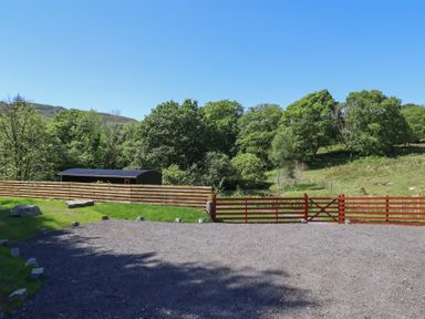 An outdoor scene with a gravel area a wooden fence a red gate and trees at Celyn in Bontddu near Dolgellau