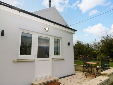 A small patio area with a wooden table and two chairs outside a white house at Orchard View in Pembroke