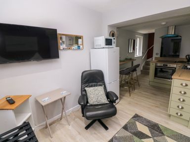A kitchen and living area with a black leather chair a white fridge with a microwave on top a wall mounted tv and a small dining table with bar stools at Orchard View in Pembroke