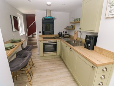 A kitchen with light green cabinets a wooden countertop stools and stairs at Orchard View in Pembroke