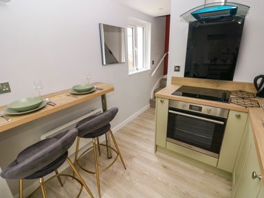 A kitchen with a built-in oven a small wooden breakfast bar with two grey bar stools at Orchard View in Pembroke