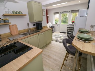 A kitchen with green cabinets and wood countertops bar stools with plates and cutlery windows and door leading outside at Orchard View in Pembroke