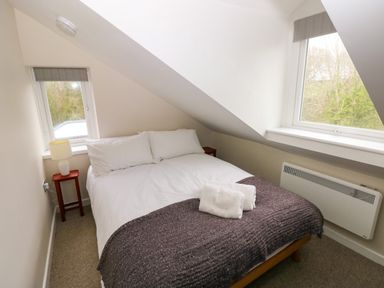A bedroom with a bed with white linens and folded towels two small windows and a bedside table with a lamp at Orchard View in Pembroke