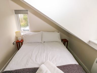 A small bedroom with a double bed white pillows and bedding two small tables a lamp and a window at Orchard View in Pembroke