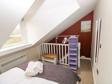 A bedroom with a bed, towels on the bed, a window, a hanging storage unit, and a small bench at Orchard View in Pembroke