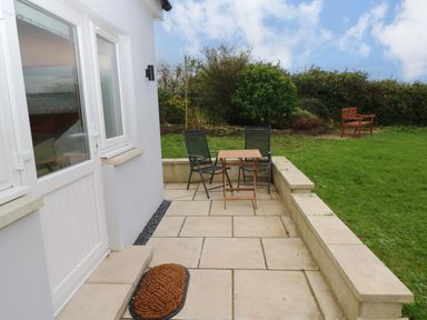 A small patio with two chairs and a wooden table next to a white door and window at Orchard View in Pembroke