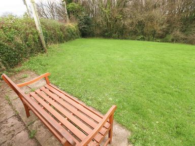 A wooden bench on a stone patio overlooking a grassy lawn with trees and bushes in the background at Orchard View in Pembroke