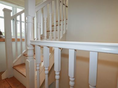 A wooden staircase with white painted balusters and handrails next to a window at Poldue House Watergate near Camelford