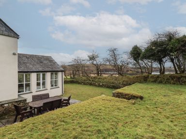 A garden with green grass and outdoor wooden table and chairs next to a cream building at Poldue House in Watergate near Camelford