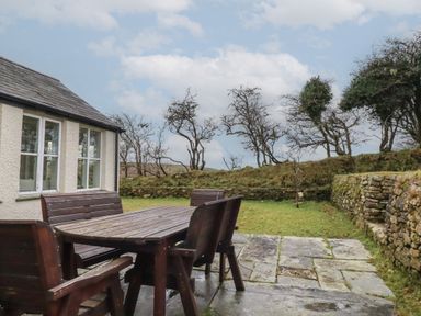 A wooden outdoor table and chairs on a stone patio next to a white building with windows and leafless trees in the background at Poldue House in Watergate near Camelford