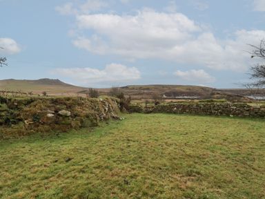 An open grassy field bordered by stone walls with hills and cloudy sky in the background at Poldue House Watergate near Camelford