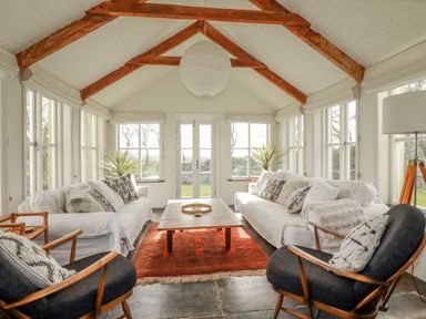 A conservatory with a sofa and armchairs at Poldue House Watergate near Camelford