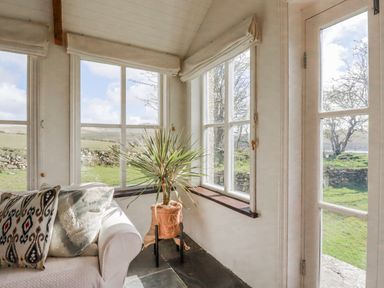 A conservatory with a plant and couch at Poldue House Watergate near Camelford