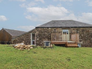 Stone barn with wooden deck door and steps on a grassy slope at Logan Barn in Poldue near Camelford